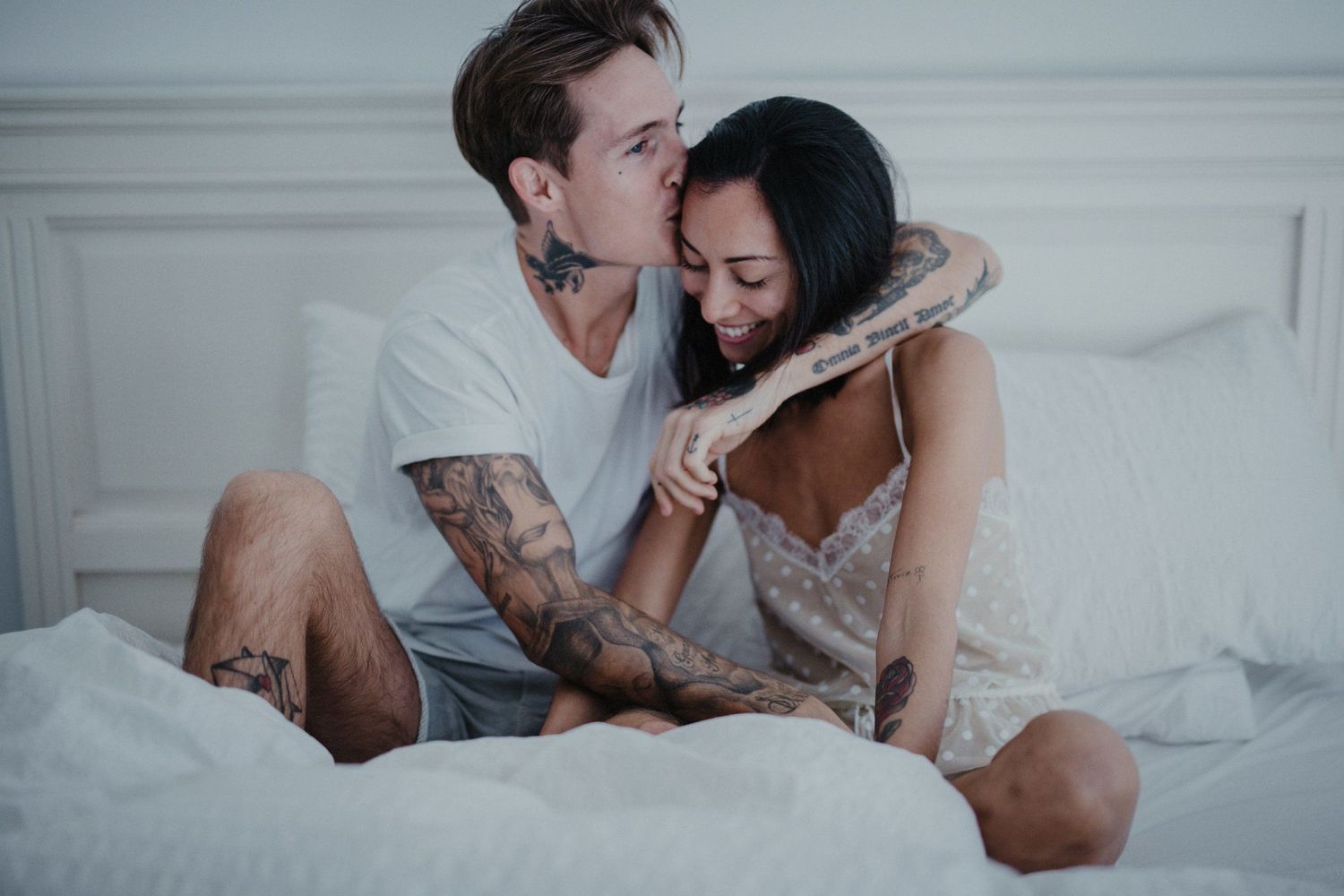 An intimate couple sharing laughter and embracing while sitting in bed.