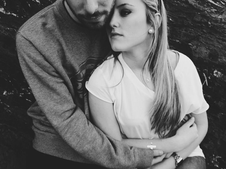Intimate black and white portrait of a couple embracing against dark background.