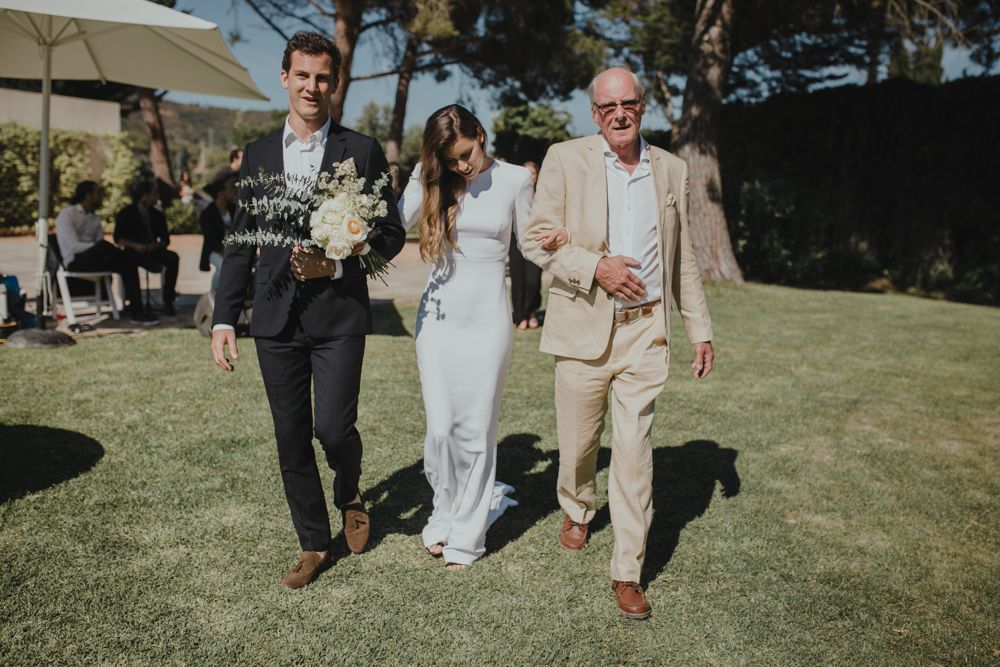 Wedding party members walking together on a sunny lawn with umbrellas in the background.
