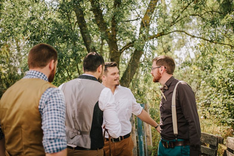 Group of men in casual attire conversing outdoors amidst trees and wooden fence.