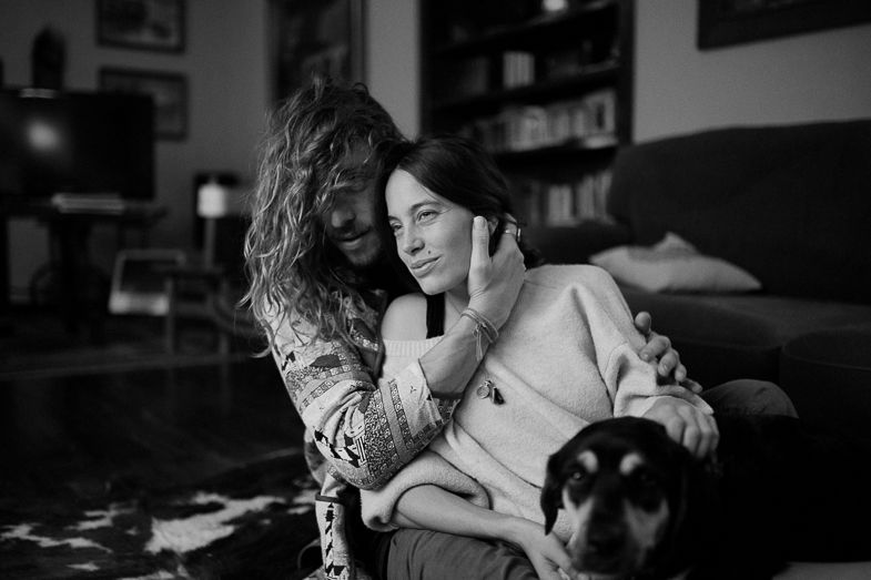 Black and white photo of two people relaxing on couch with small dog in living room setting.
