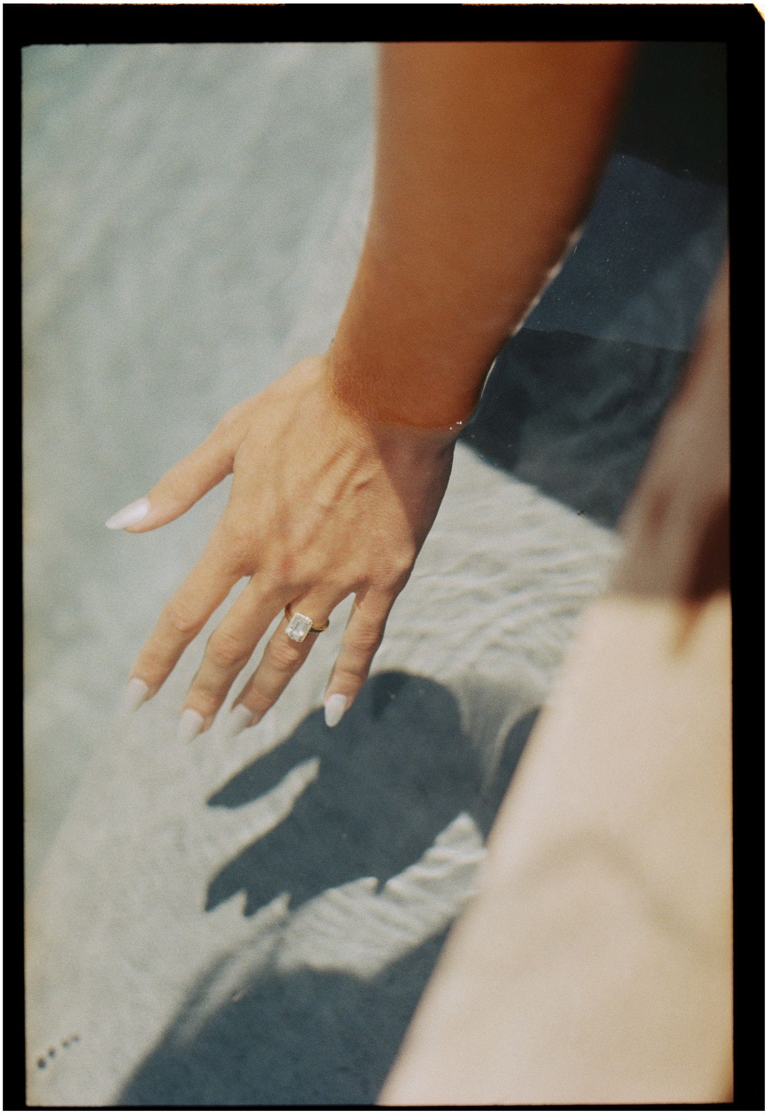 Close-up of bride's hand showing engagement ring with shadow on light surface.