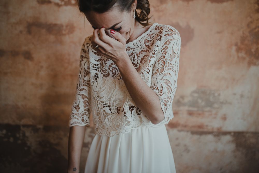 A delicate lace wedding dress bodice with three-quarter length sleeves against a rustic textured wall.