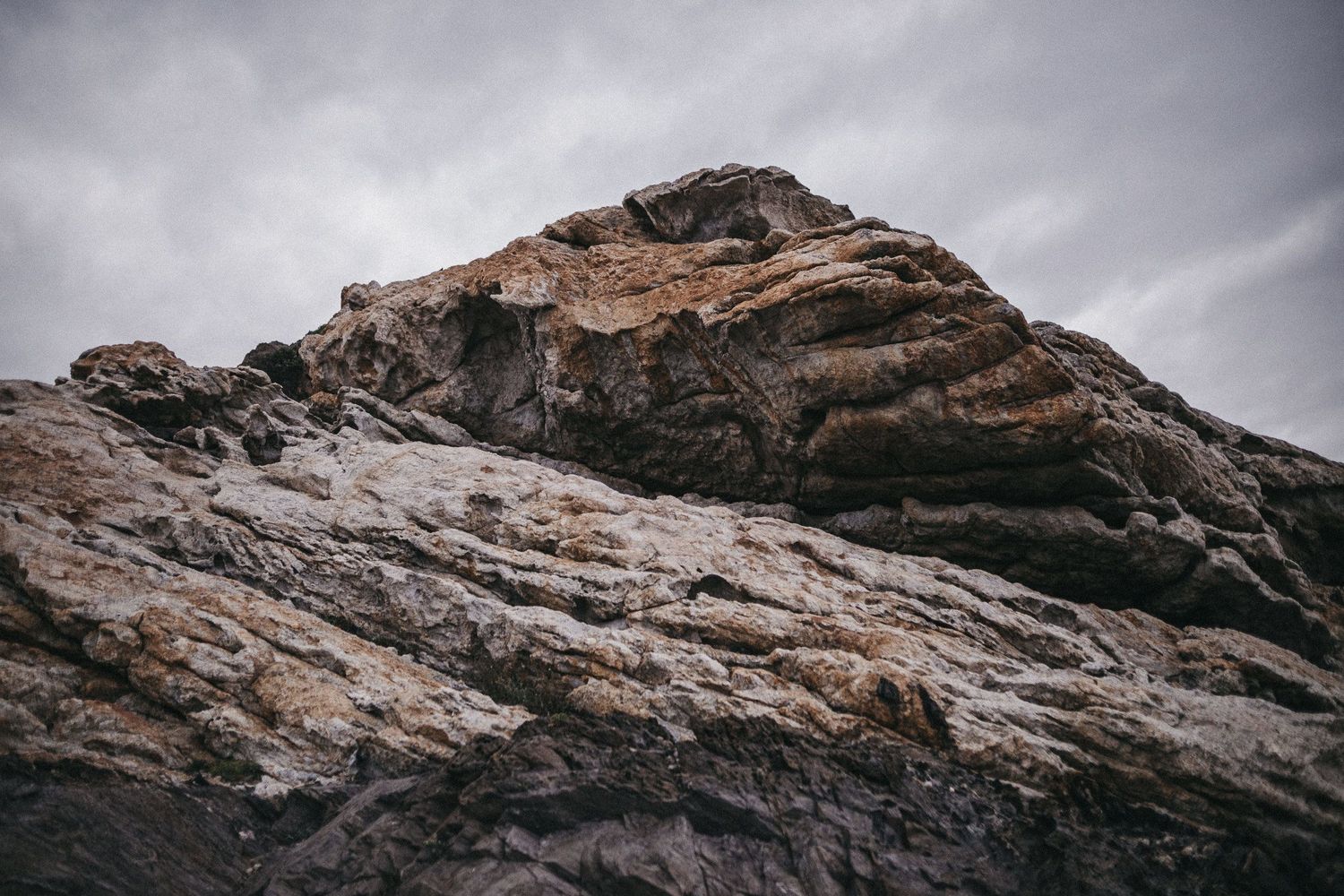 A dramatic rocky mountain peak under stormy gray skies.