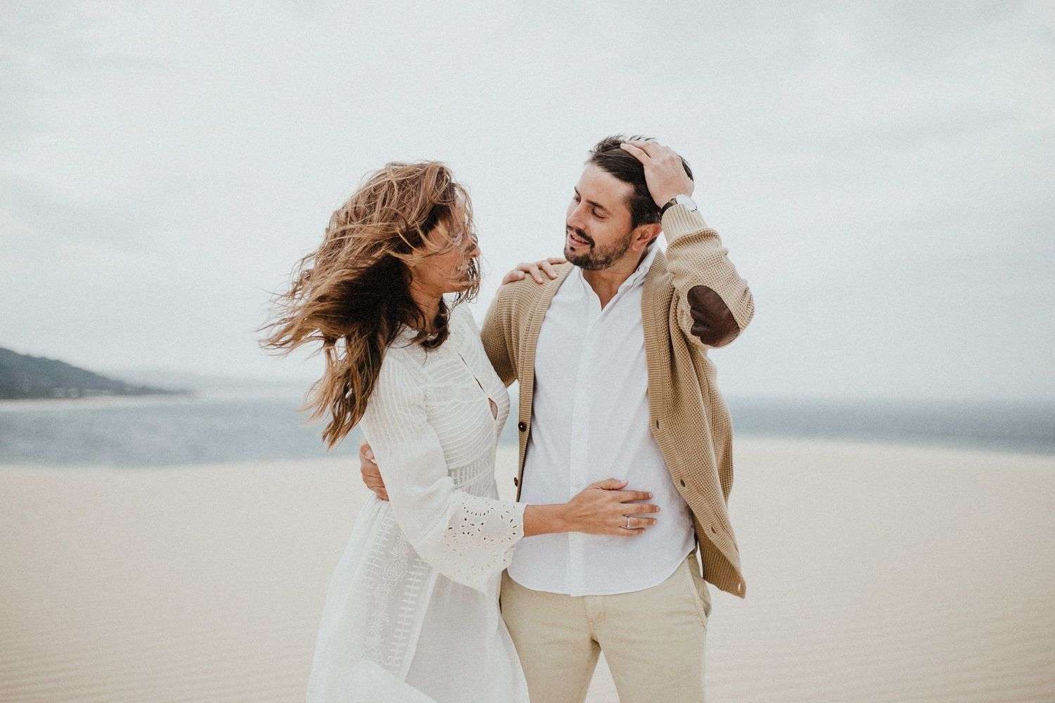 Carefree couple laughing together on windswept beach dunes.