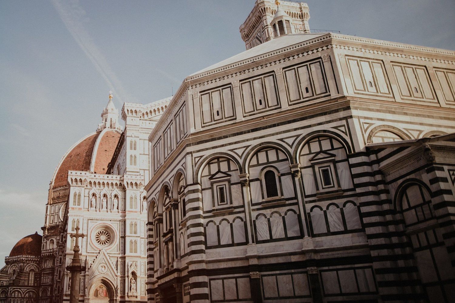 The stunning marble facade of Florence Cathedral with its iconic dome against a bright sky.
