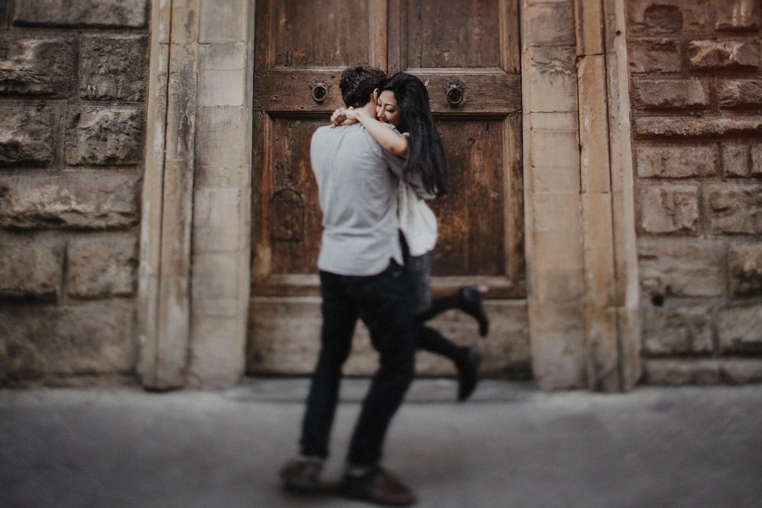 Playful couple embracing in front of historic church doorway.