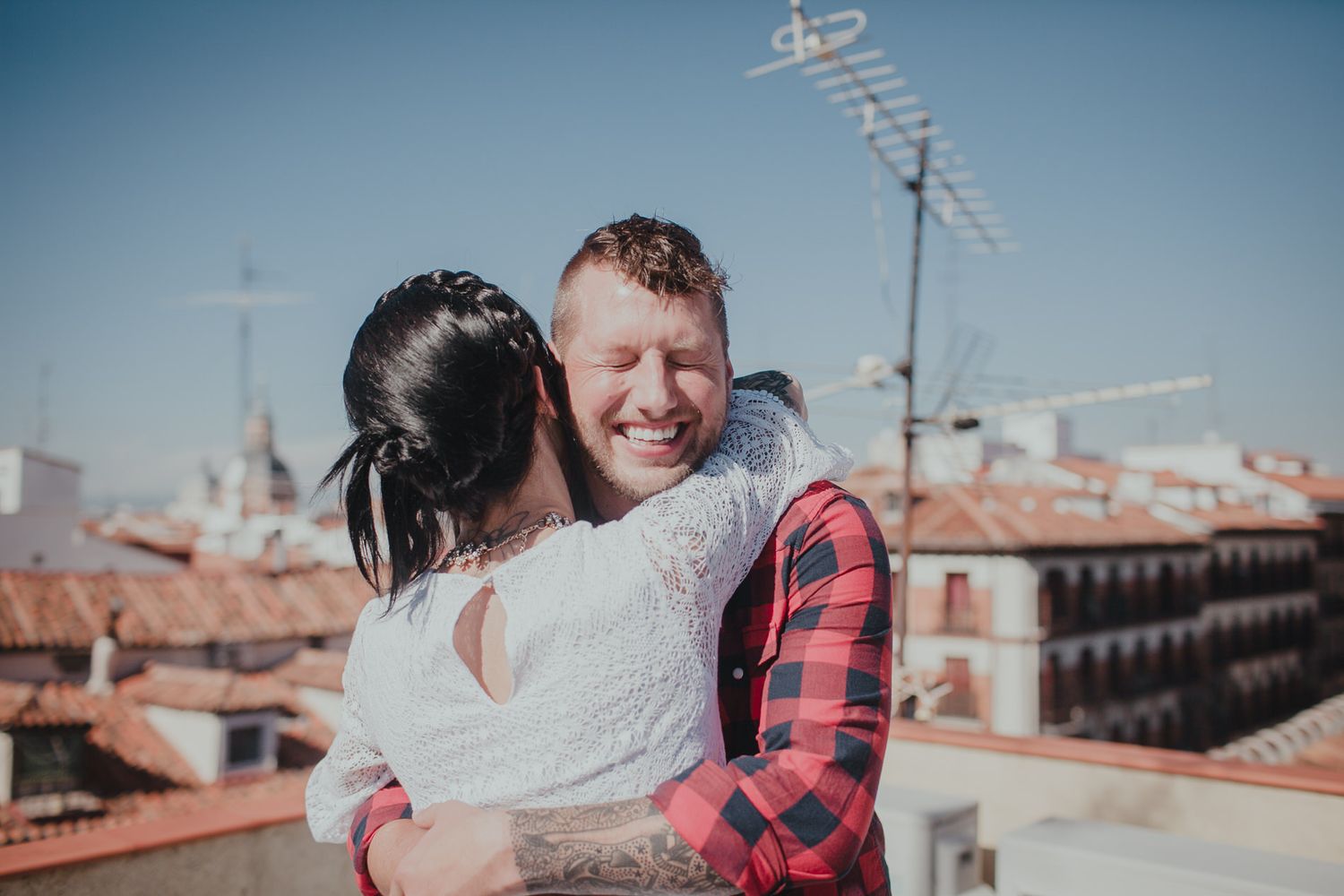 A loving embrace between a couple on a rooftop overlooking traditional Spanish architecture.