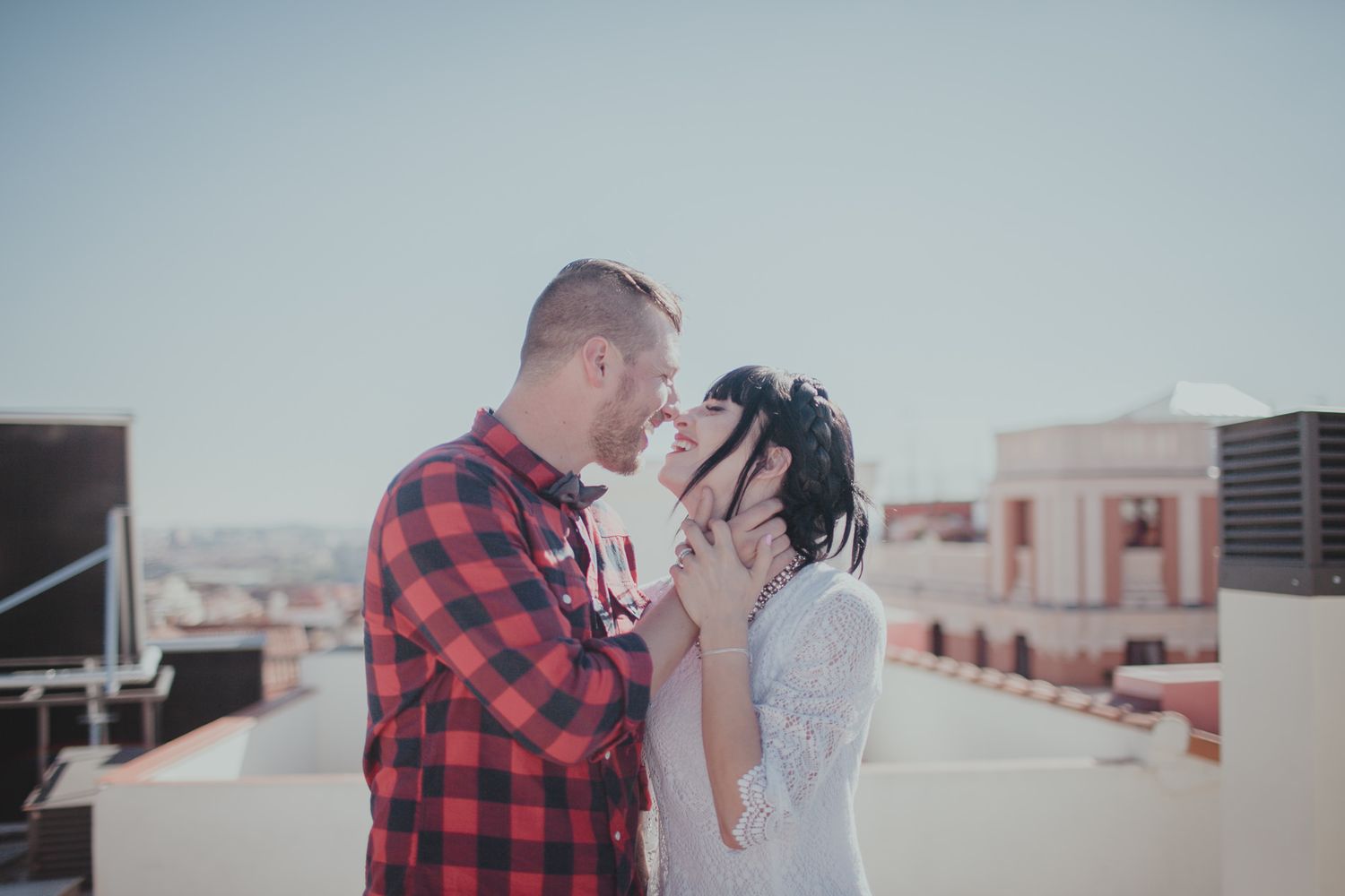 Tender moment between couple in casual wear on sunny urban rooftop.