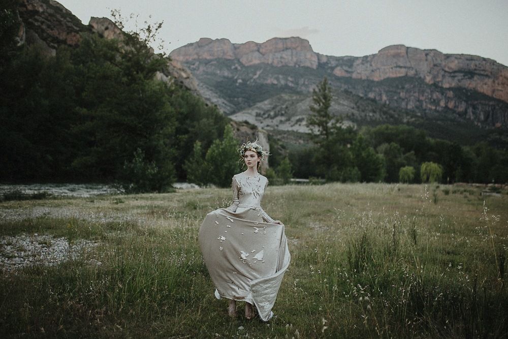 Ethereal white dress flows in a mountain meadow at dusk with dramatic peaks in the background.