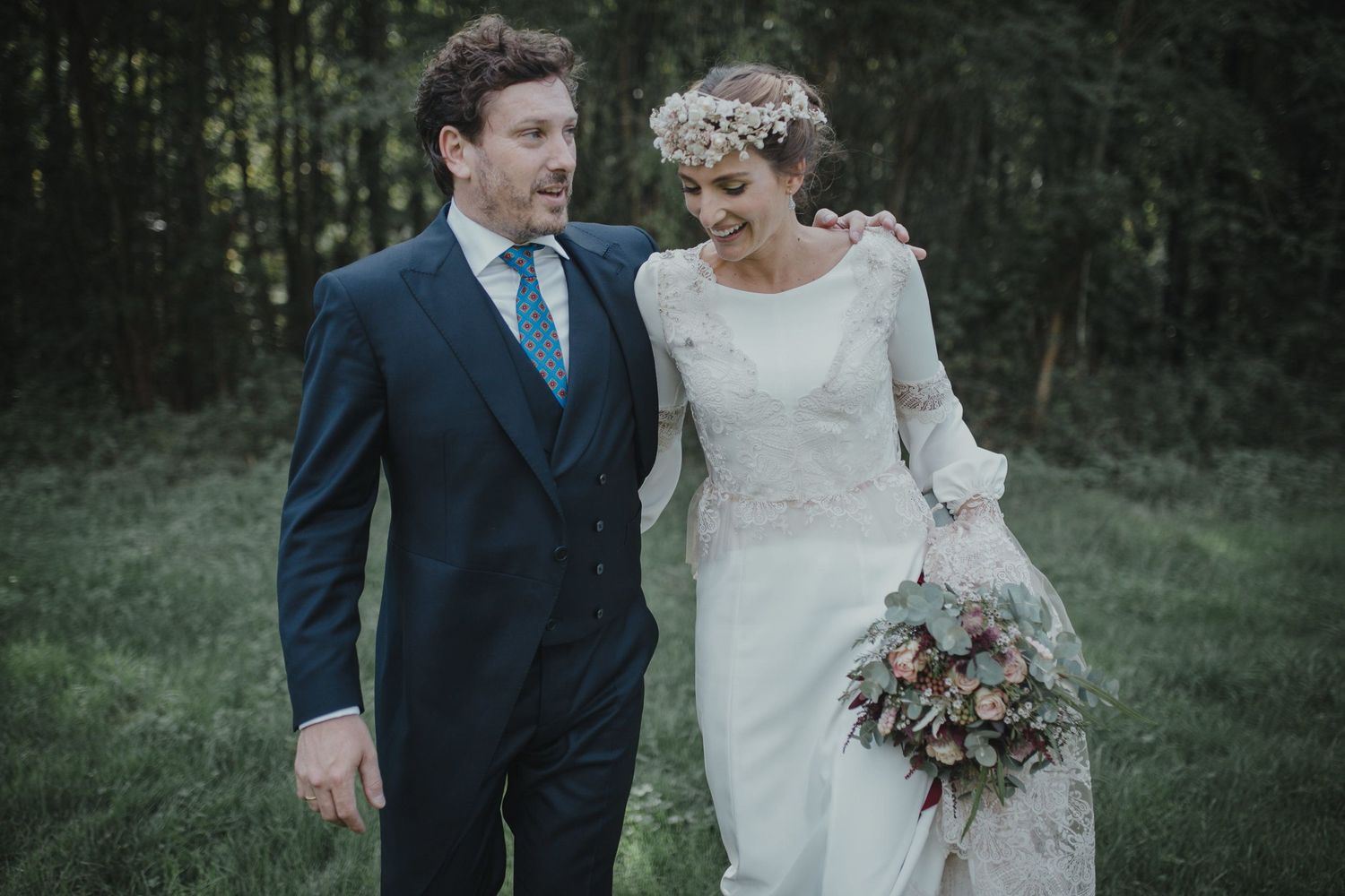 Elegant couple in vintage-inspired wedding attire walking through garden setting.