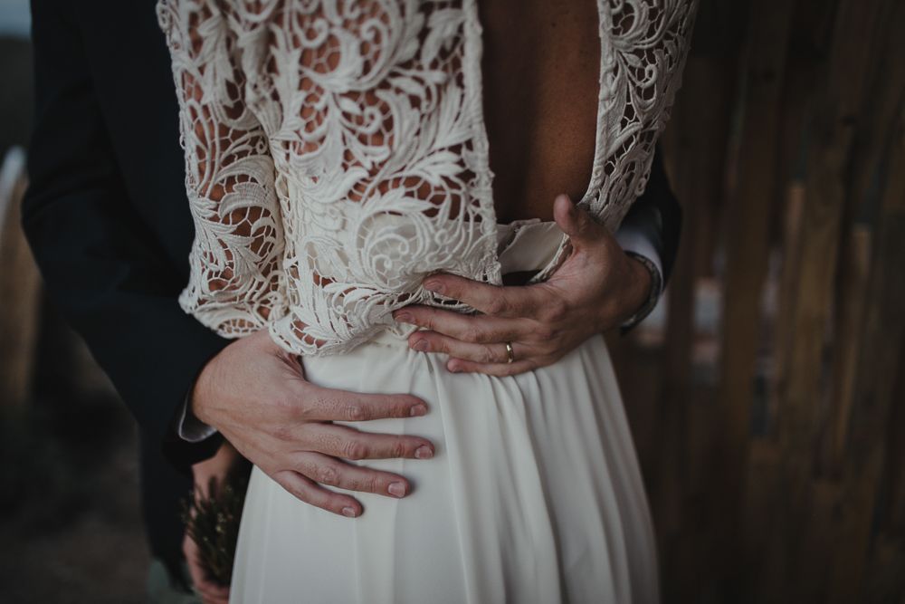 Close up detail of hands gently holding delicate white lace and flowy fabric of a wedding dress.