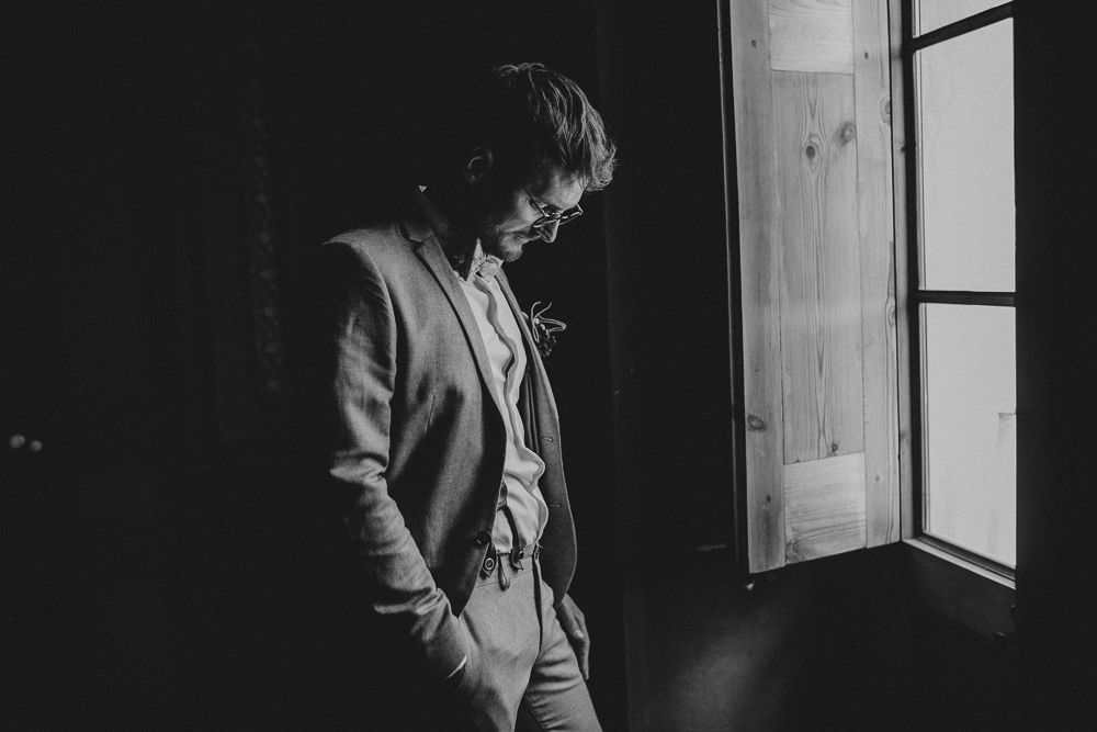 Dramatic black and white portrait of figure standing by window in formal attire.