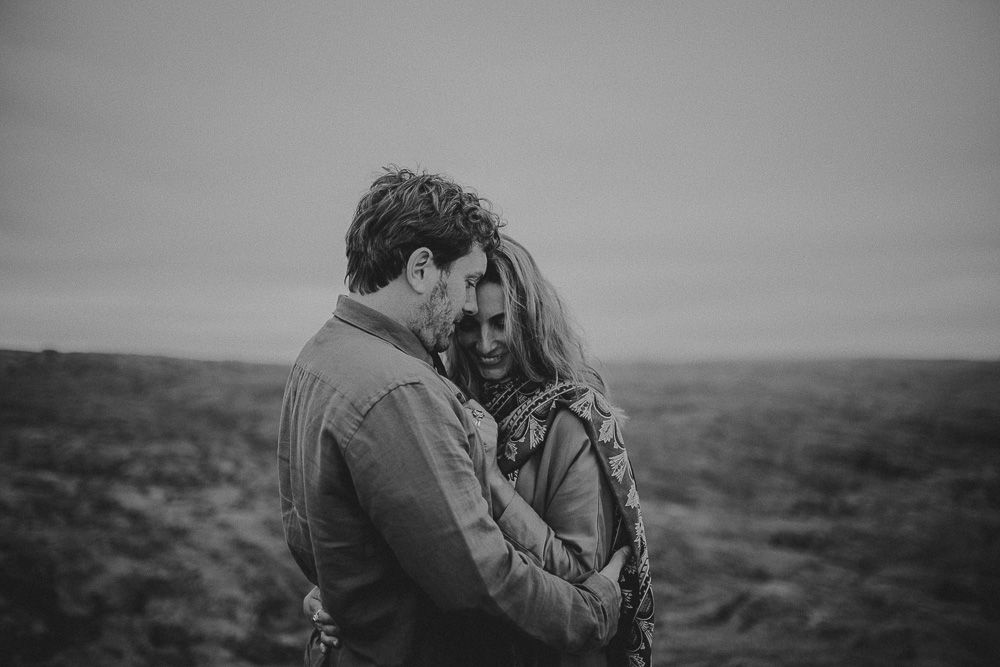 A tender black and white moment captured between two people on a misty hillside.