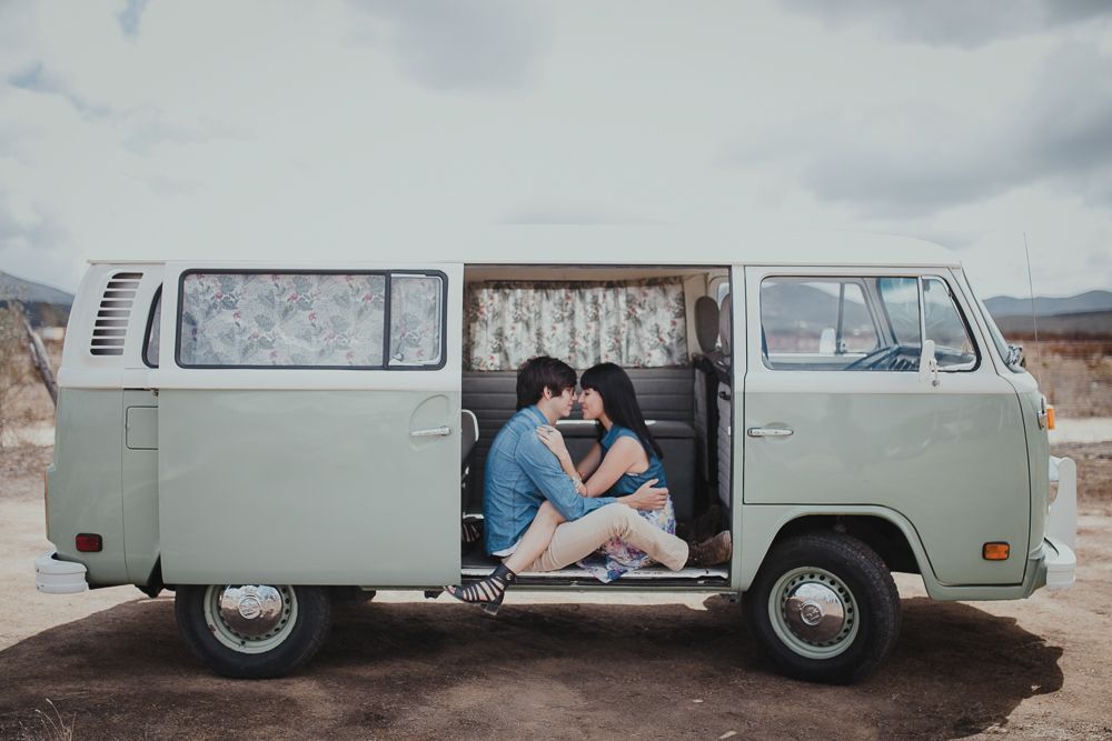A classic VW van parked in a desert landscape with a couple sharing an intimate moment inside.