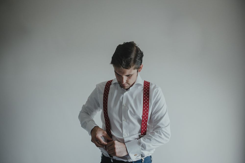 Figure in white shirt and red suspenders looking down while getting dressed.