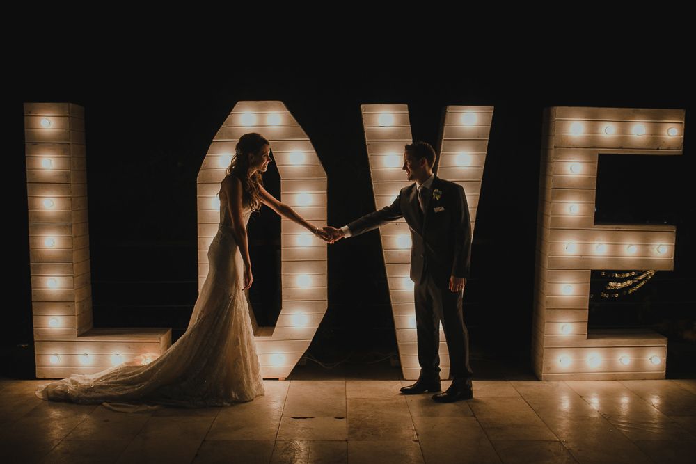 Dramatic silhouette of couple standing in front of illuminated LOVE marquee letters.