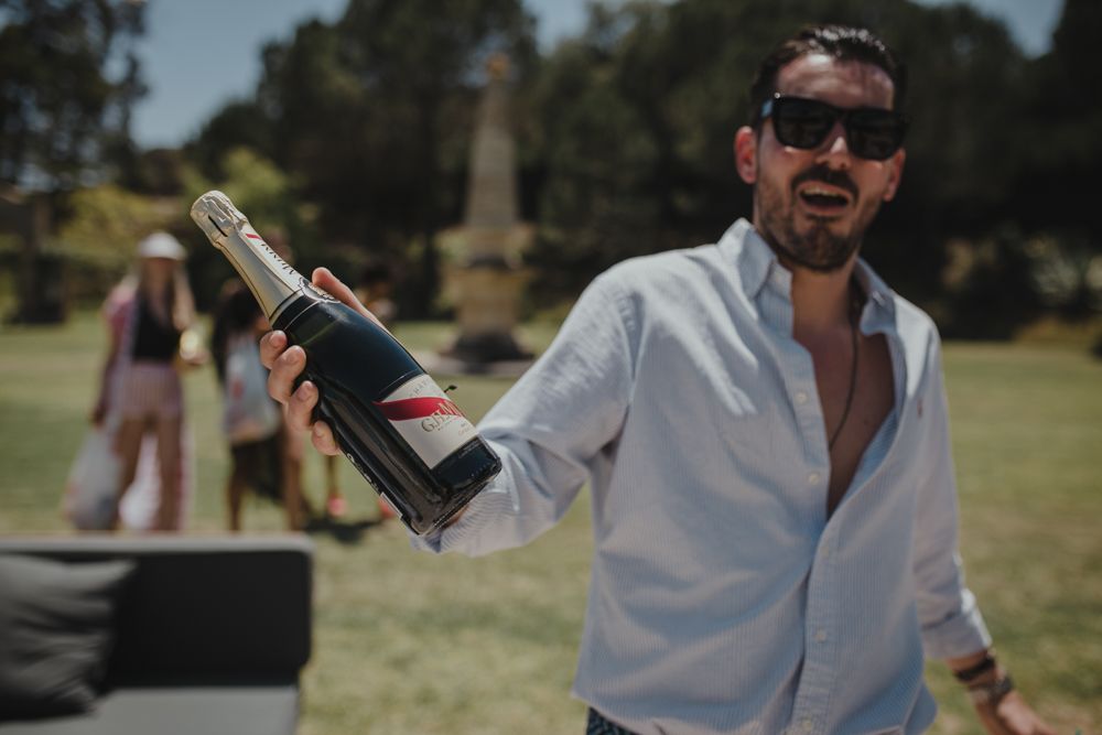 Person in white shirt holding champagne bottle at outdoor celebration.