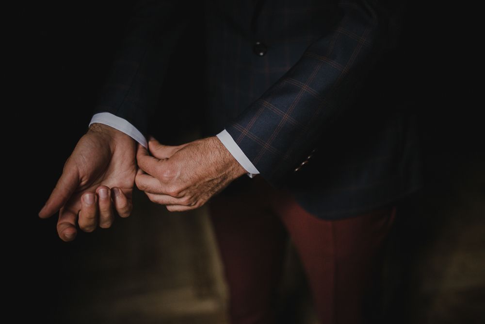 Close-up of hands adjusting suit cuffs in moody dramatic lighting.