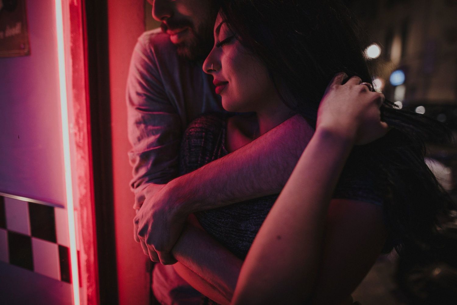 An intimate embrace captured in red neon lighting against a dark background.