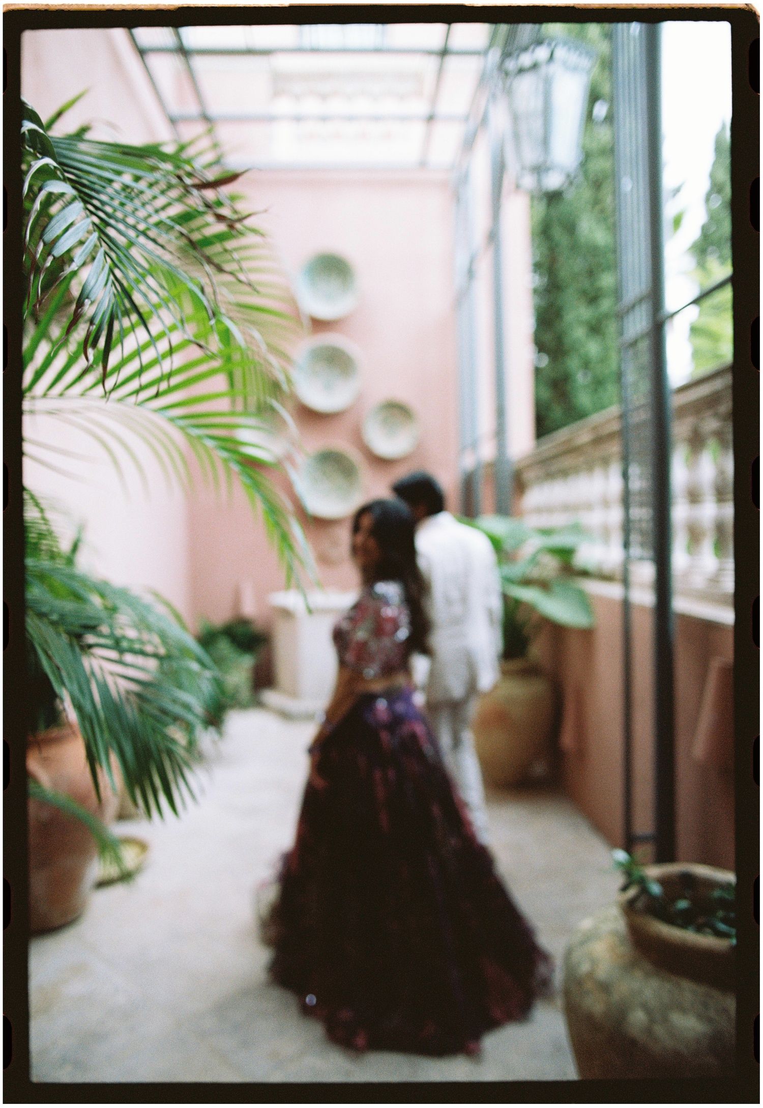 Soft-focus film photograph of Elina and Jag walking away through a courtyard with plants.