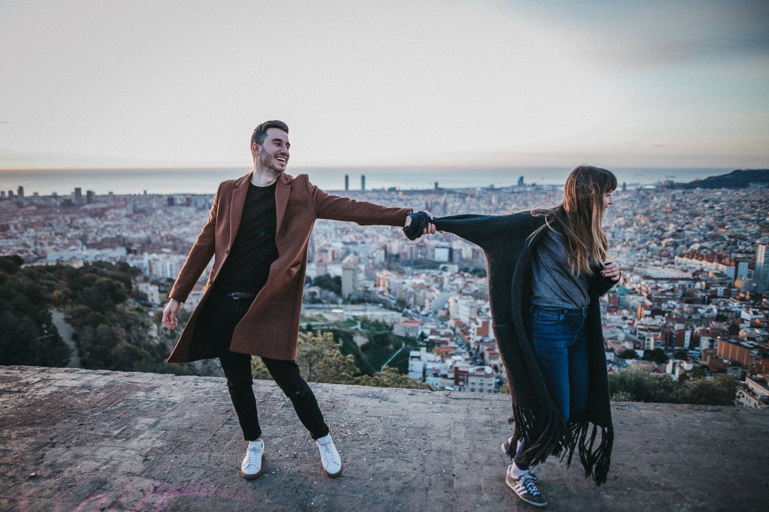 Playful couple holding hands against Barcelona cityscape panorama.