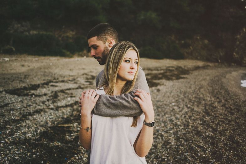 A couple in casual attire standing together in a natural outdoor setting with dry grass and mountains.