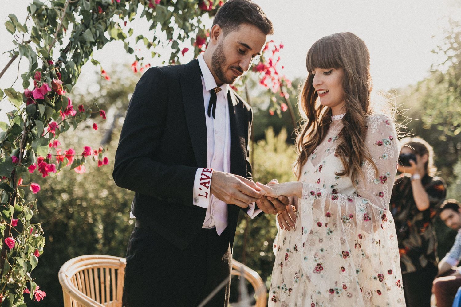 A couple shares an intimate moment in a garden setting surrounded by pink flowers and natural sunlight.
