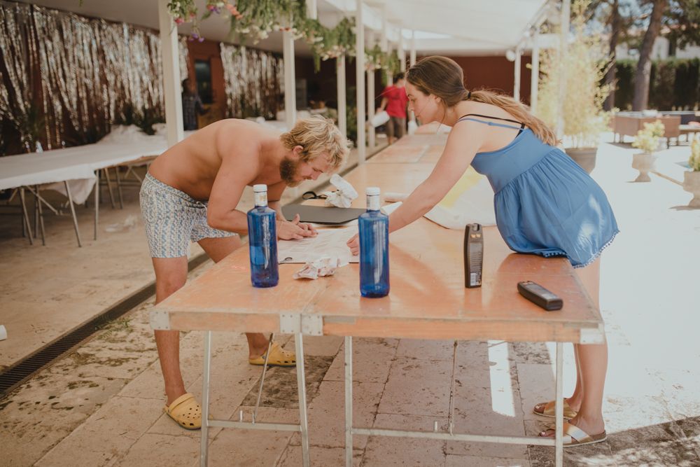 Players participating in a beer pong game setup with blue cups on a wooden table outdoors at a party.
