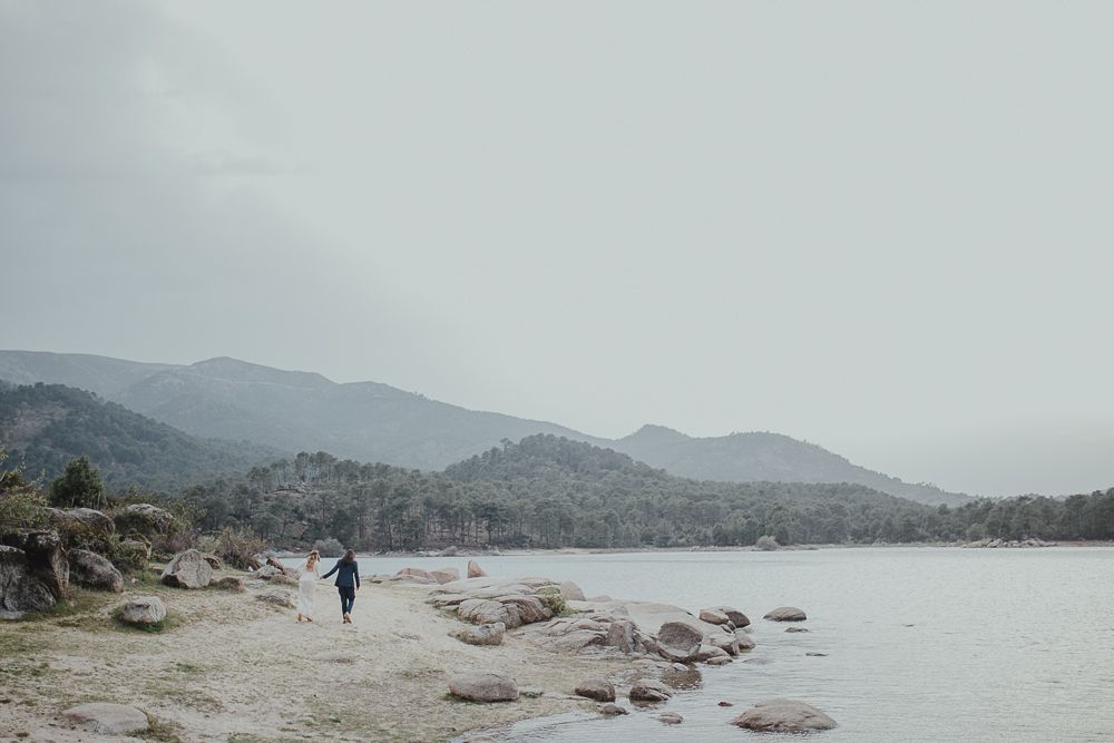 Person walking alone on rocky beach with misty mountains in distance.