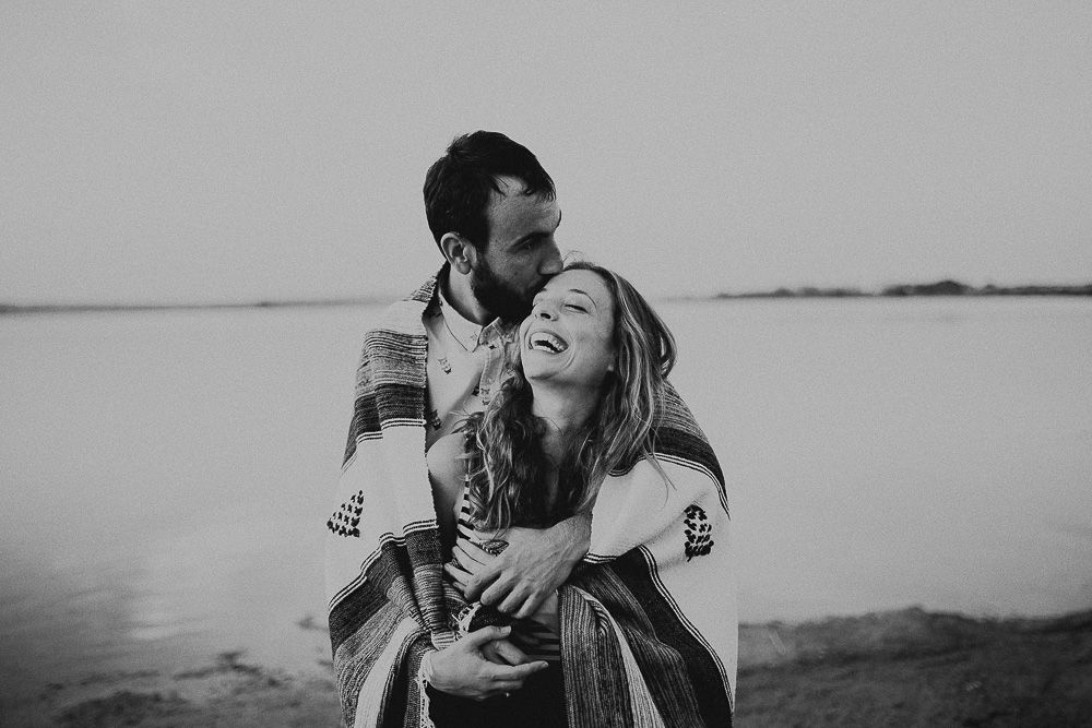 Black and white portrait of loving couple laughing together by lakeside.