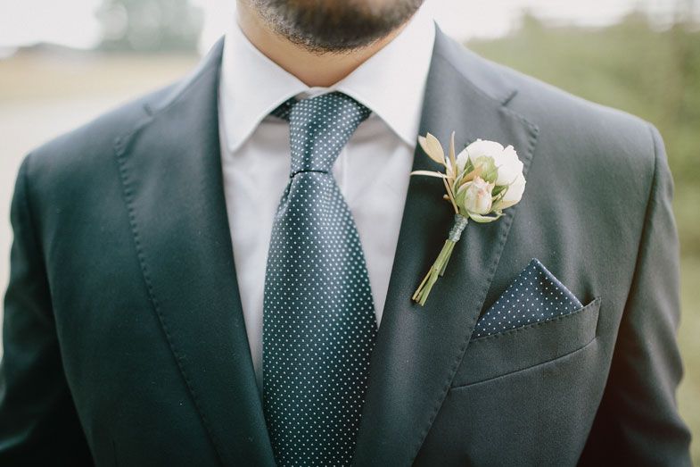 Close-up of a groom's formal attire featuring a navy suit, patterned tie, and white boutonniere.