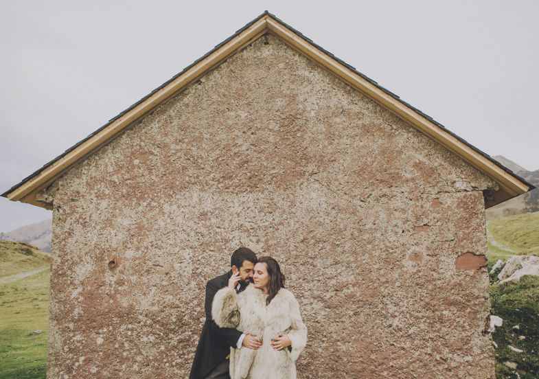 A couple poses intimately against the rustic backdrop of a stone building.