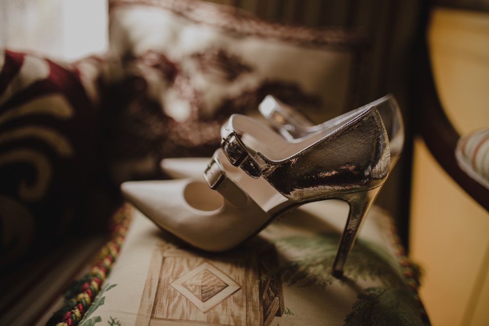 A stylish white and silver wedding heel shoe photographed against a textured background.