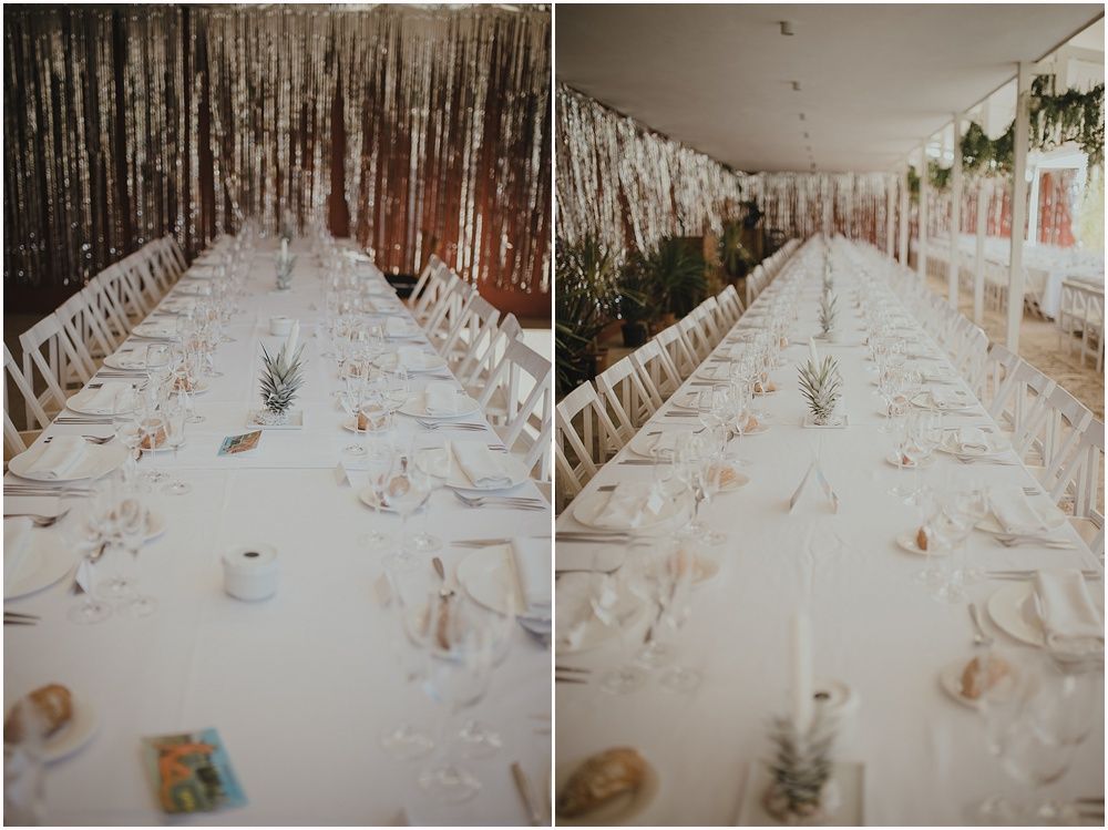 Long dining table set with white linens and place settings under metallic streamers.