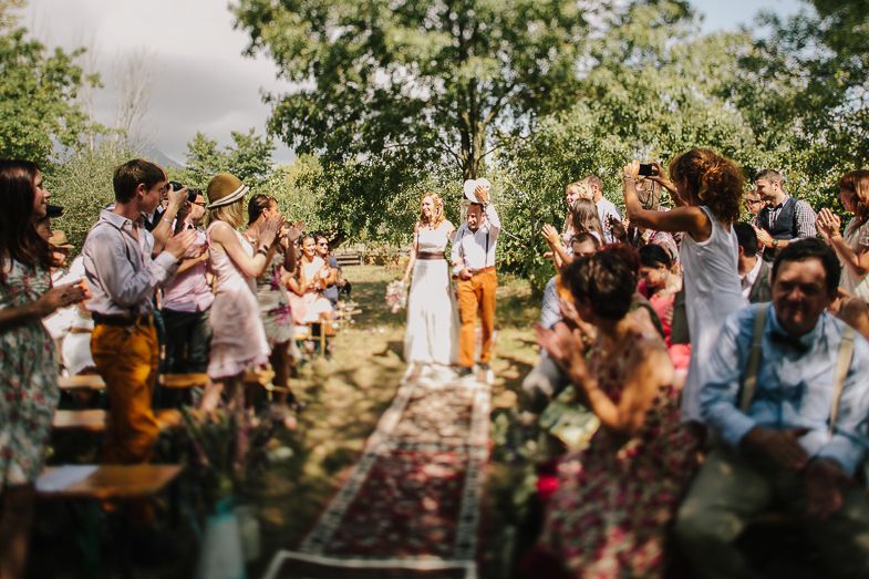 Wedding guests clapping during an outdoor forest ceremony with vintage rugs on the ground.
