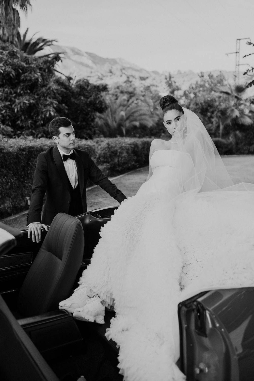 Black and white photos of a couple posing with a classic car in formal wedding attire.