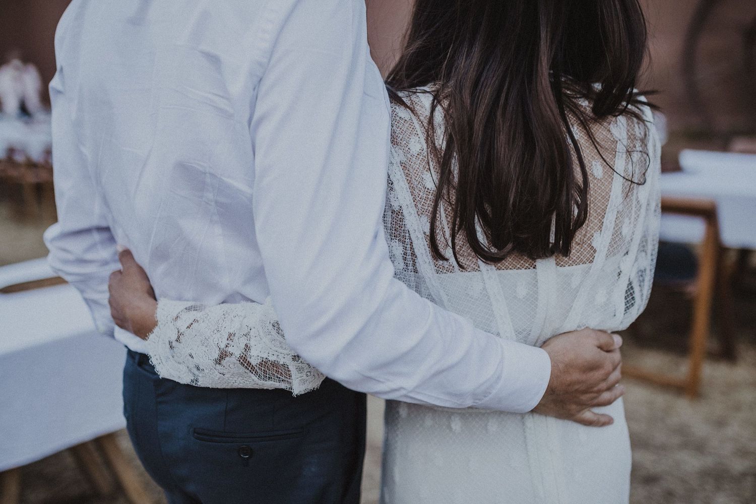 A romantic embrace captured in soft focus showing white lace and formal attire.