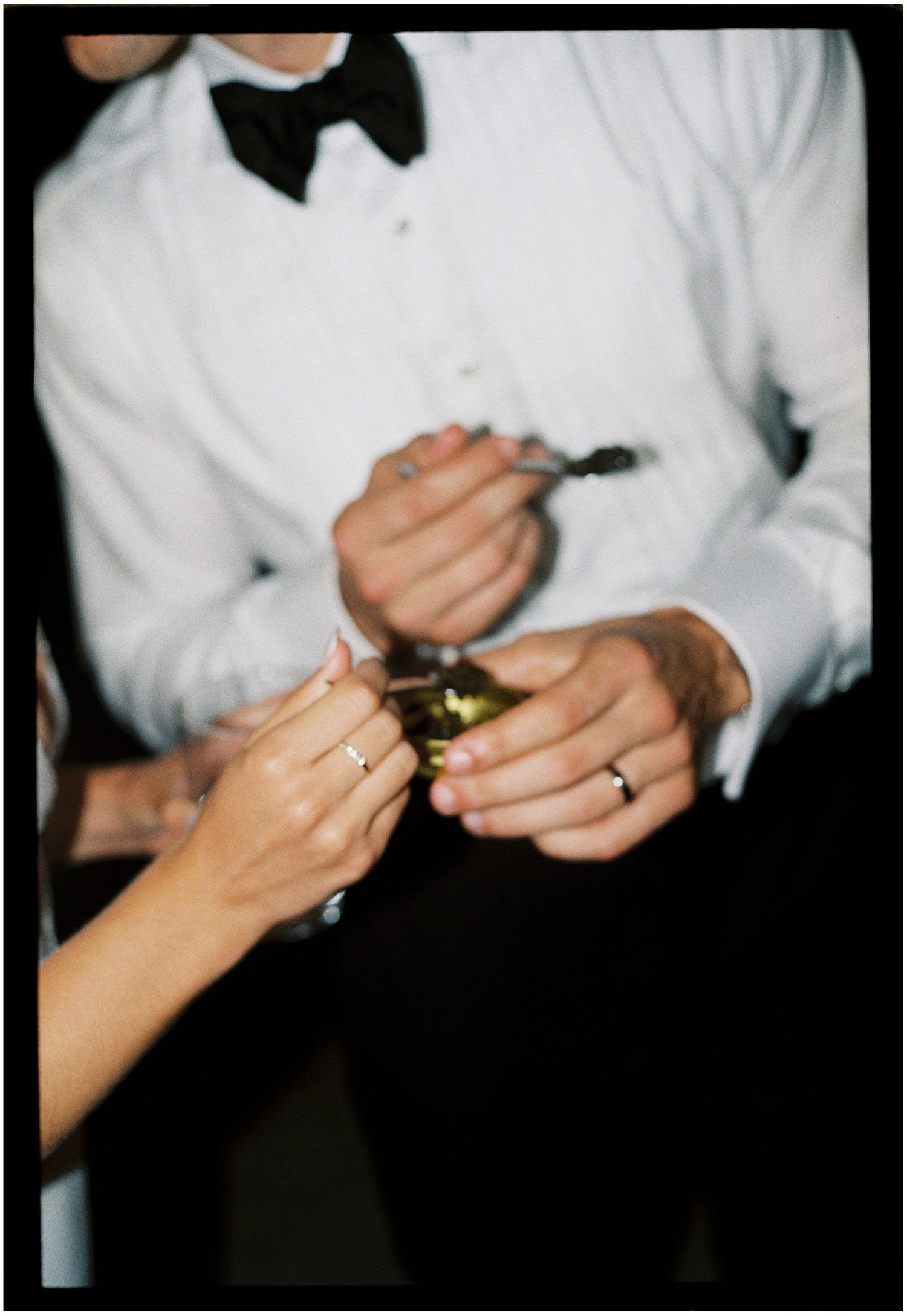Close-up of hands opening a champagne bottle with person wearing white dress shirt and black bow tie.