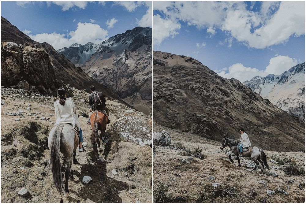 Horseback riders traverse a rocky mountain trail surrounded by towering peaks.