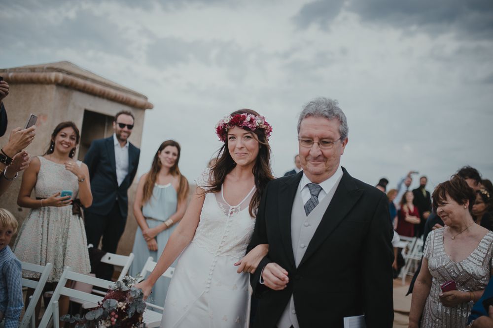 Wedding ceremony procession on a Mediterranean terrace under cloudy skies.