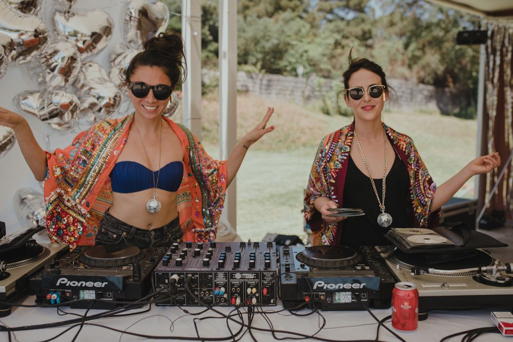 Two DJs performing at an outdoor event with professional mixing equipment and colorful kimono style outfits.