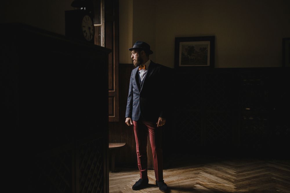 Silhouette of person in suit and hat standing by window in dark room.