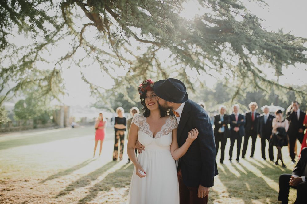 An intimate outdoor wedding moment with guests looking on in the background.