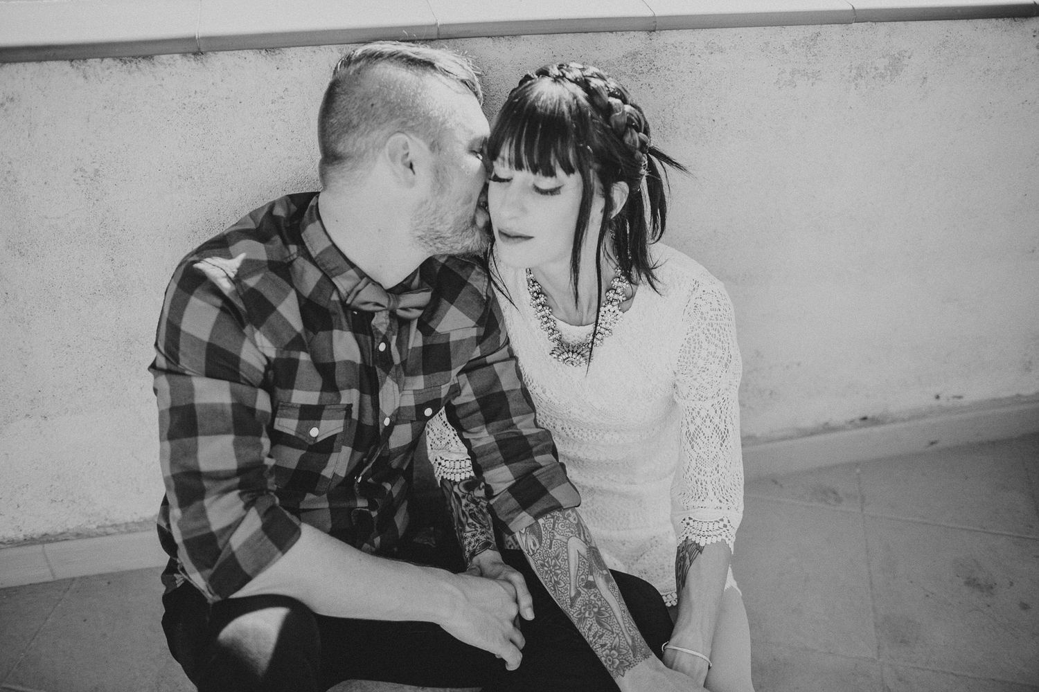 Intimate black and white portrait of couple in casual attire against plain wall.