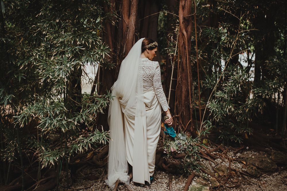 Wedding couple poses in a lush forest setting wearing elegant white attire.