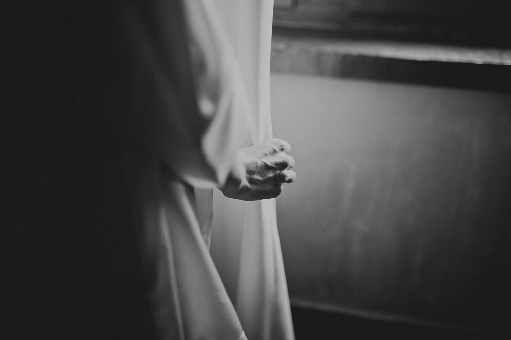 Dramatic black and white close-up of hands grasping white fabric near a window.