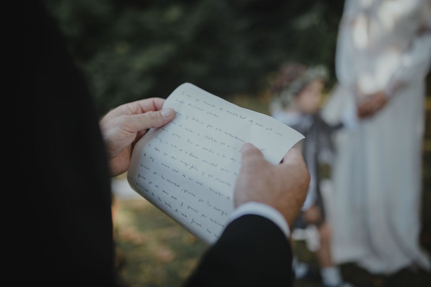 Close-up of hands holding handwritten vows during outdoor wedding ceremony.