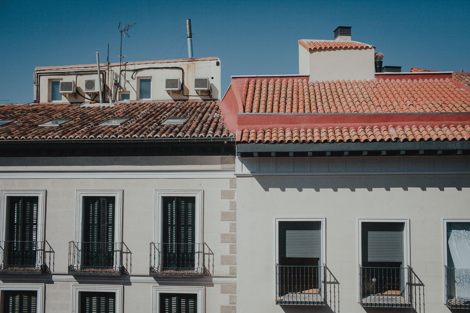 Mediterranean style buildings with terracotta roofs and white walls against bright blue sky.