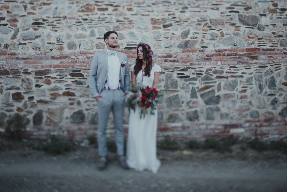 A newlywed couple stands together against a stone wall backdrop in moody lighting.